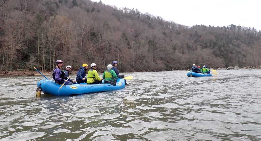 Two rafts are full of people wearing life jackets as they move down a river. 